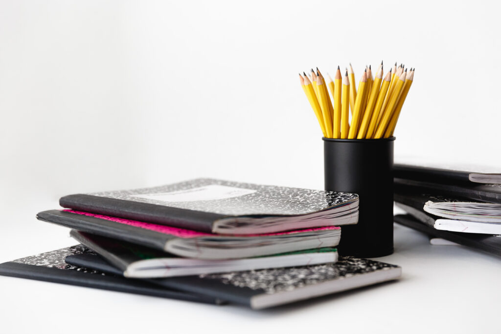 Pile of composition notebooks and cup with yellow pencils
