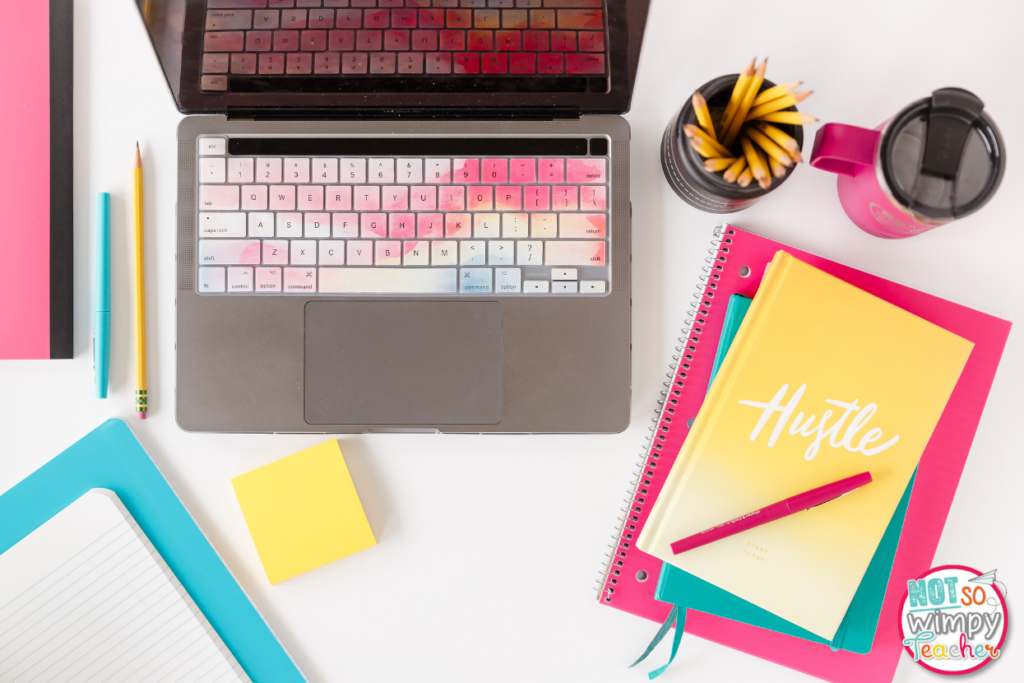 Flat lay of a laptop, cup of pencils, jug of water, notebooks, and more.